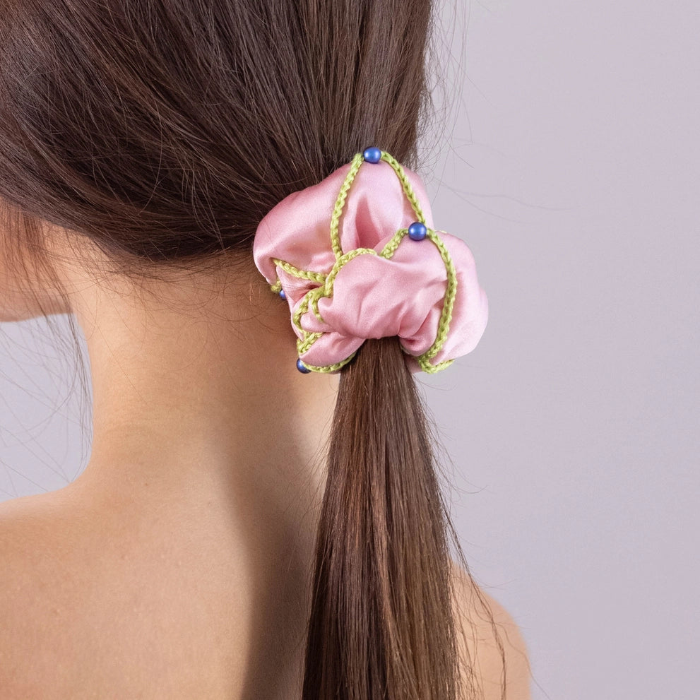 
                  
                    A dark-haired woman, view from the back, with stylish ponytail is wearing Malkiele designer pink silk scrunchie, embellished with 6 white pearls from Swarovski and light green silk knit ribbon, name Majestic.
                  
                