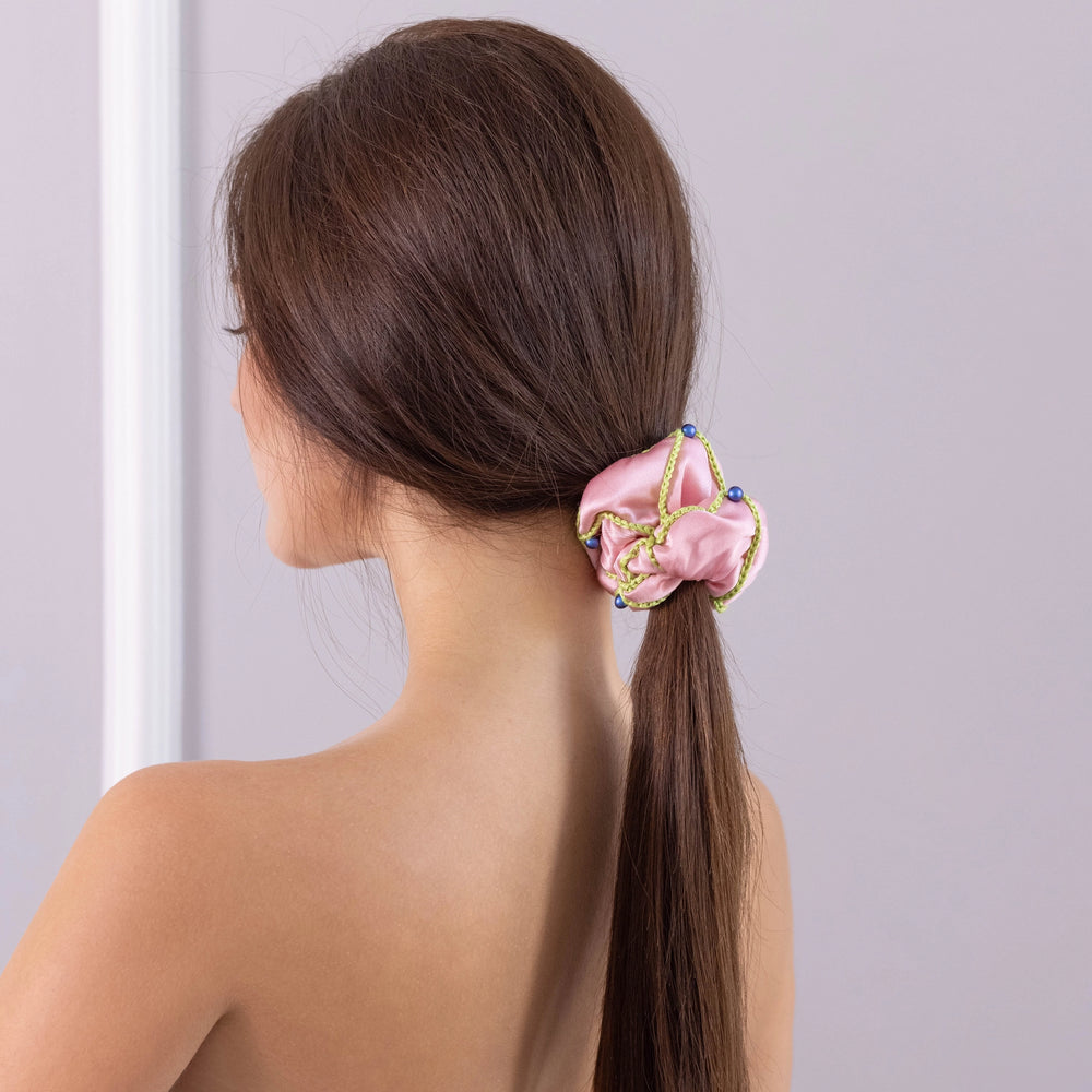 
                  
                    A dark-haired woman, view from the back, with stylish ponytail is wearing Malkiele designer pink silk scrunchie, embellished with 6 white pearls from Swarovski and light green silk knit ribbon, name Majestic.
                  
                