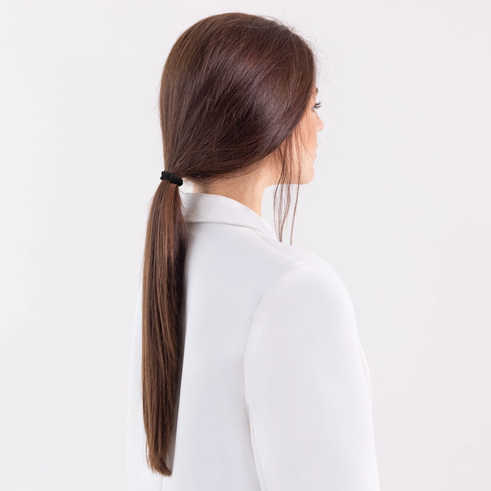 A dark-haired girl in white jacket, view from the back, with classic ponytail is wearing Malkiele designer bridal black silk gentle hair tie, name Finesse.