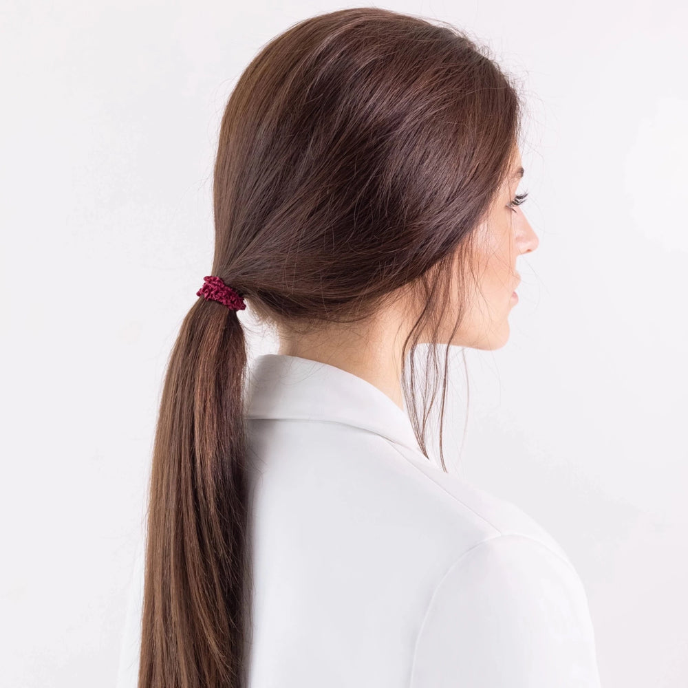 
                  
                    A dark-haired girl in white jacket with ponytail is wearing Malkiele designer burgundy silk gentle hair tie, name Finesse.
                  
                