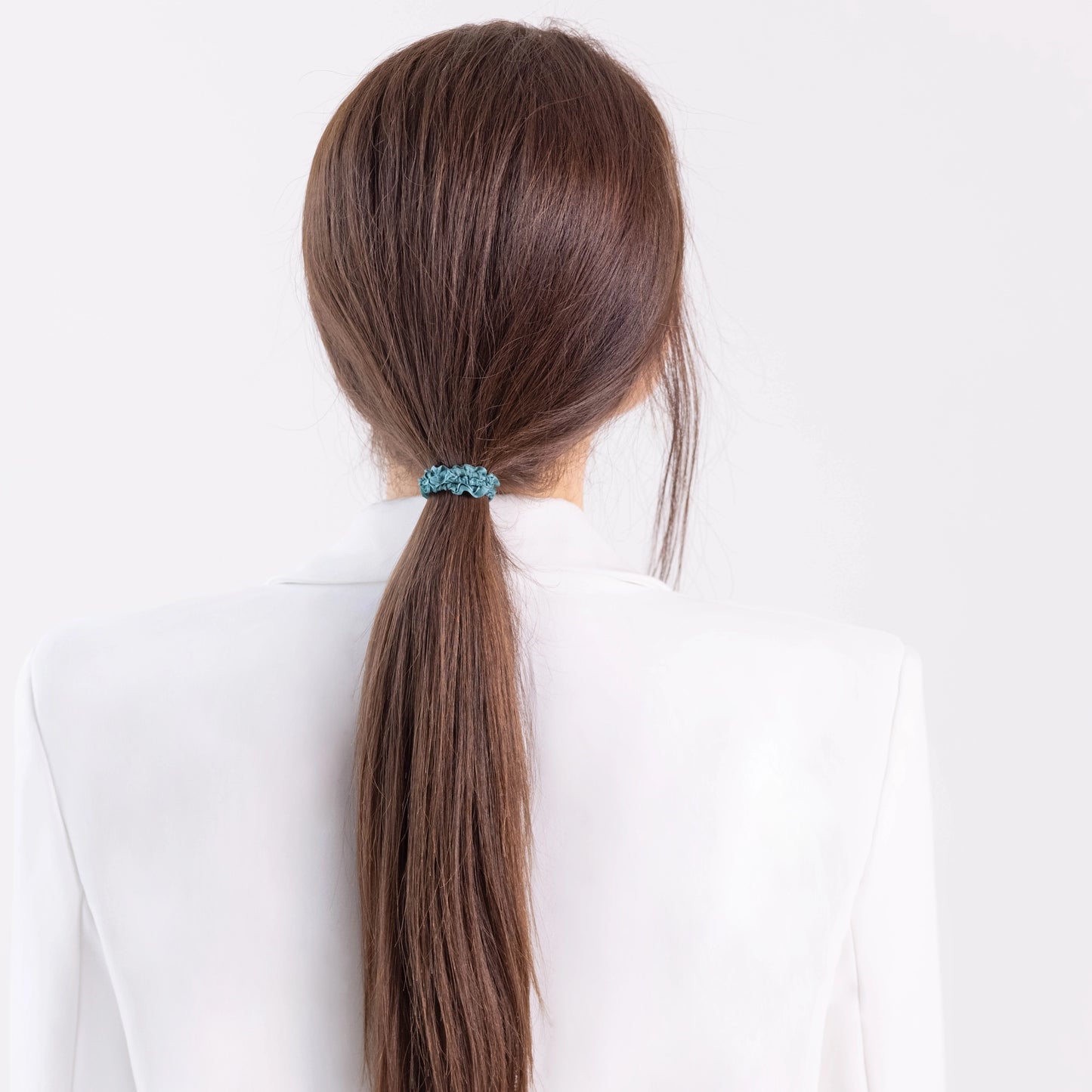 A dark-haired girl in white jacket, view from the back, with ponytail is wearing Malkiele designer green silk gentle hair tie, name Finesse.