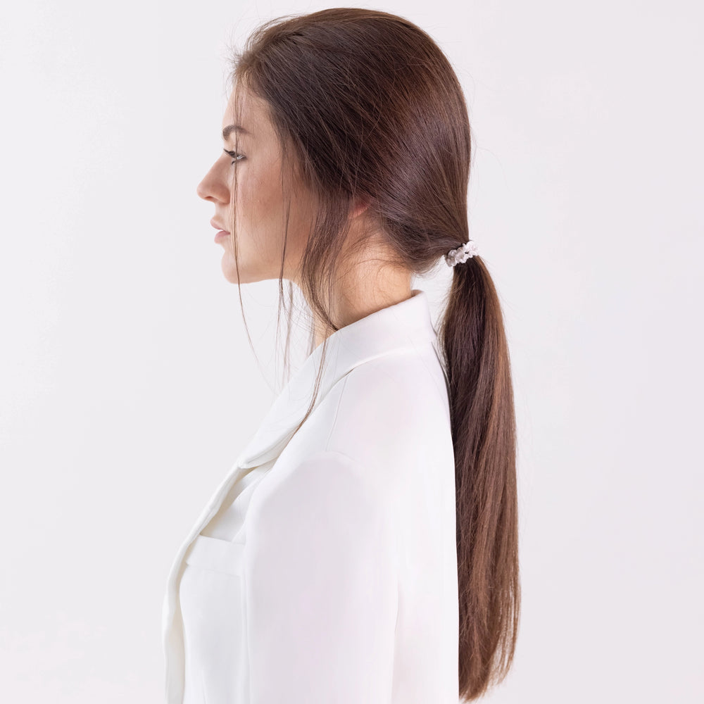 
                  
                    A dark-haired girl in white jacket, side view with half face, with long classic ponytail is wearing Malkiele designer bridal white silk gentle hair tie, name Finesse.
                  
                