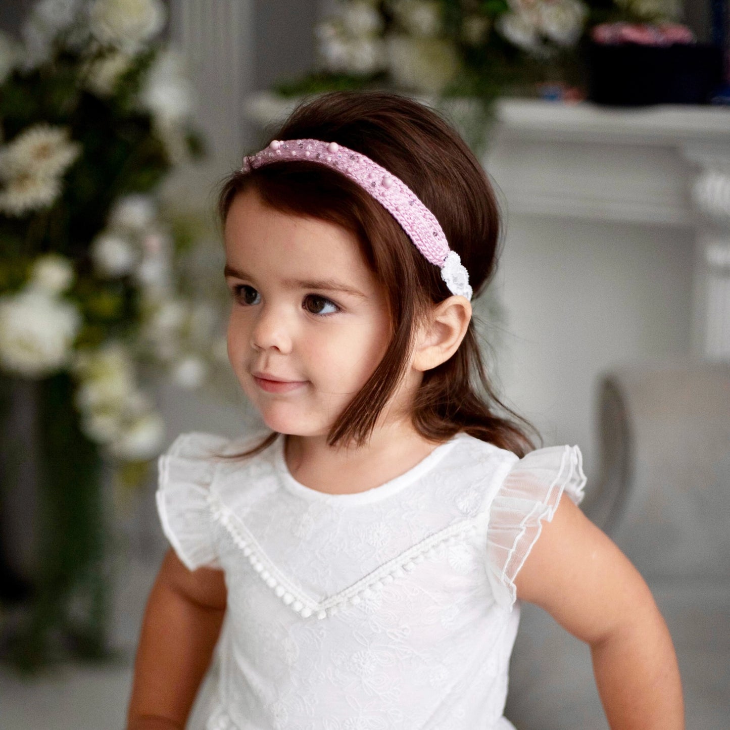 Dark-haired smiling little girl in white dress is wearing pink silk knit headband, embellished with pearls from Swarovski® and white lace, Malkiele designer, name Sweetheart.