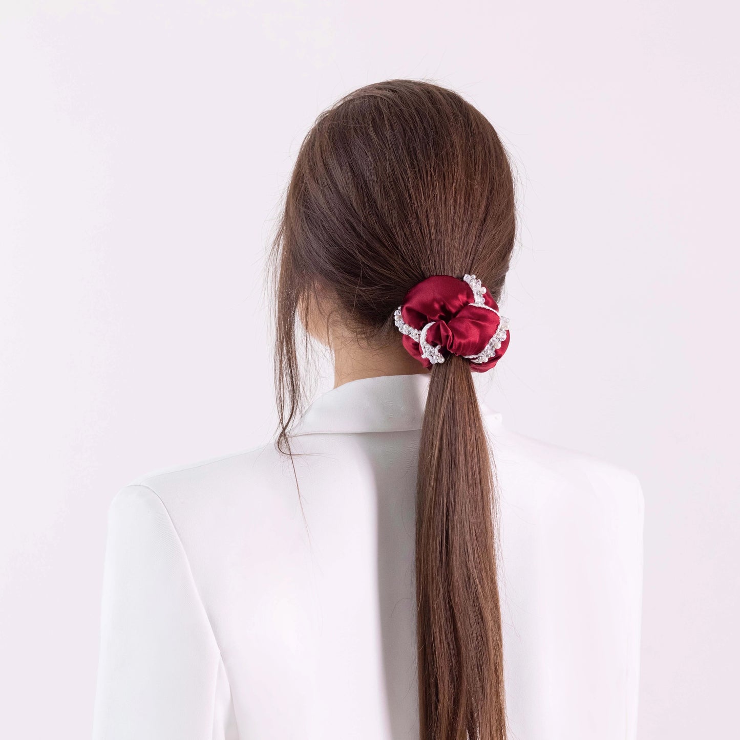 Dark-haired girl in white jacket, from behind, with stylish ponytail is wearing Malkiele designer burgundy silk scrunchie, embellished with crystals from Swarovski® and white silk knit ribbon, name Elizabeth.