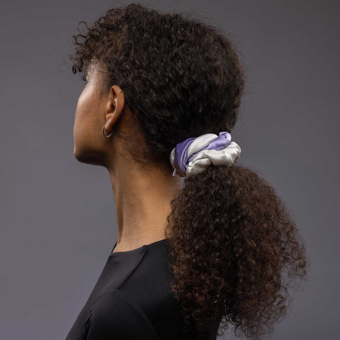 
                  
                    A dark-haired African woman is wearing Malkiele silk scrunchie in white and lavender, name Marianne
                  
                