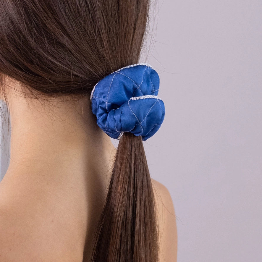 
                  
                    A dark-haired woman, view from the back, with stylish ponytail is wearing Malkiele designer royal blue silk scrunchie, embellished grey silk knit ribbon, name Morning Passion.
                  
                