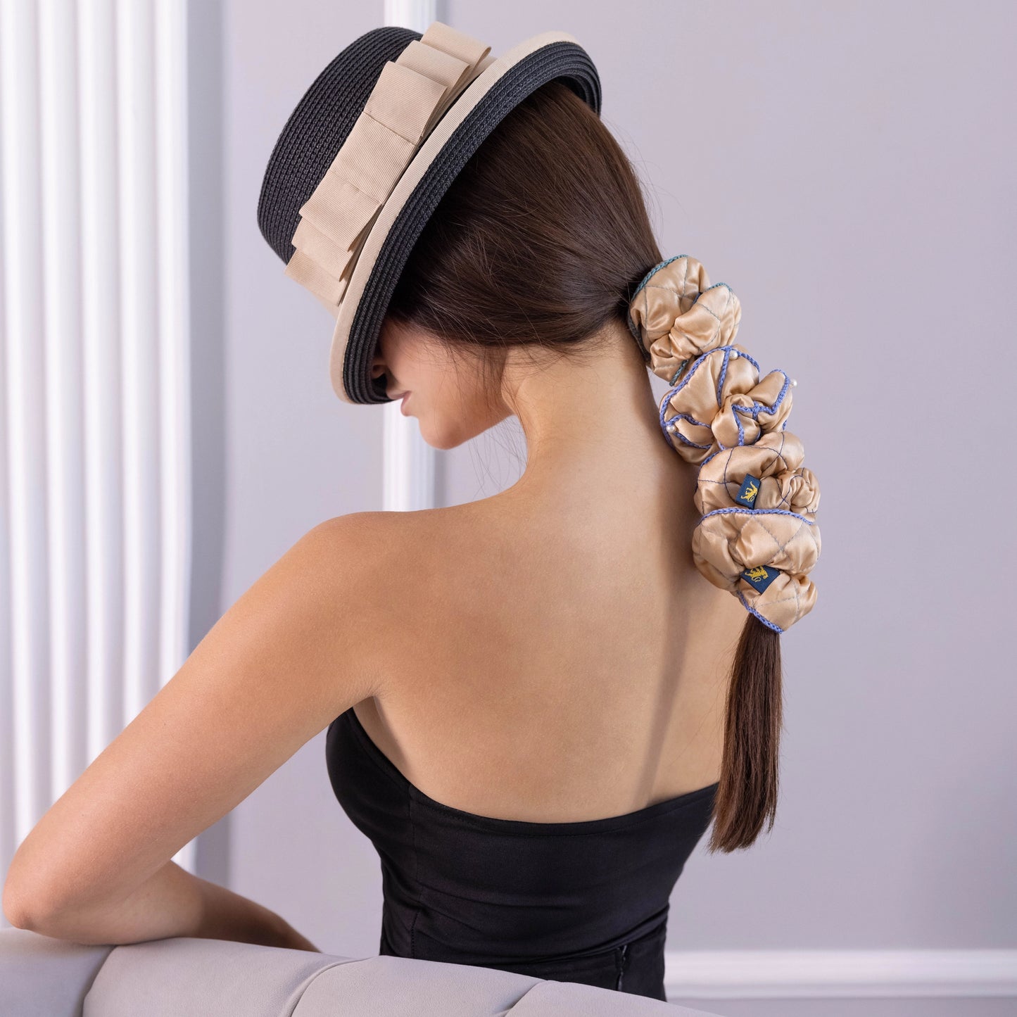 
                  
                    A dark-haired woman in hat, side view, half the face, with stylish ponytail is wearing Malkiele designer beige silk scrunchies set, embellished light blue silk knit ribbon, name Morning Passion.
                  
                