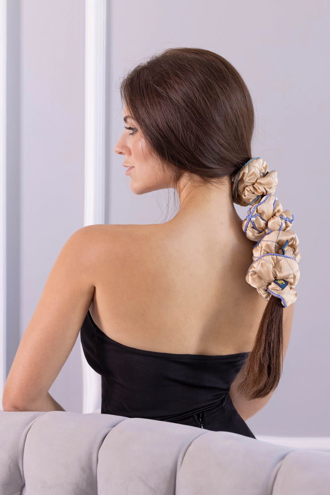 
                  
                    A dark-haired woman, side view, half the face, with stylish ponytail is wearing Malkiele designer beige silk scrunchies set, embellished light blue silk knit ribbon, name Morning Passion.
                  
                