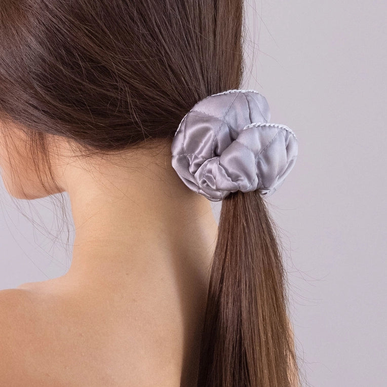 
                  
                    A dark-haired woman, view from the back, with stylish ponytail is wearing Malkiele designer grey silk scrunchie, embellished white silk knit ribbon, name Morning Passion.
                  
                