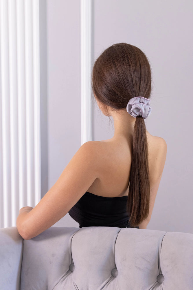 
                  
                    A dark-haired woman, view from the back, with stylish ponytail is wearing Malkiele designer grey silk scrunchie, embellished pink silk knit ribbon, name Morning Passion.
                  
                