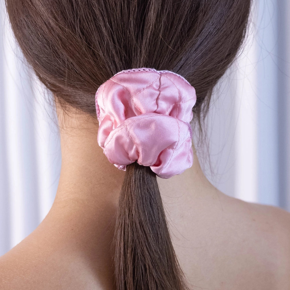 
                  
                    A dark-haired woman, view from the back, with stylish ponytail is wearing Malkiele designer pink silk scrunchie, embellished pink silk knit ribbon, name Morning Passion.
                  
                