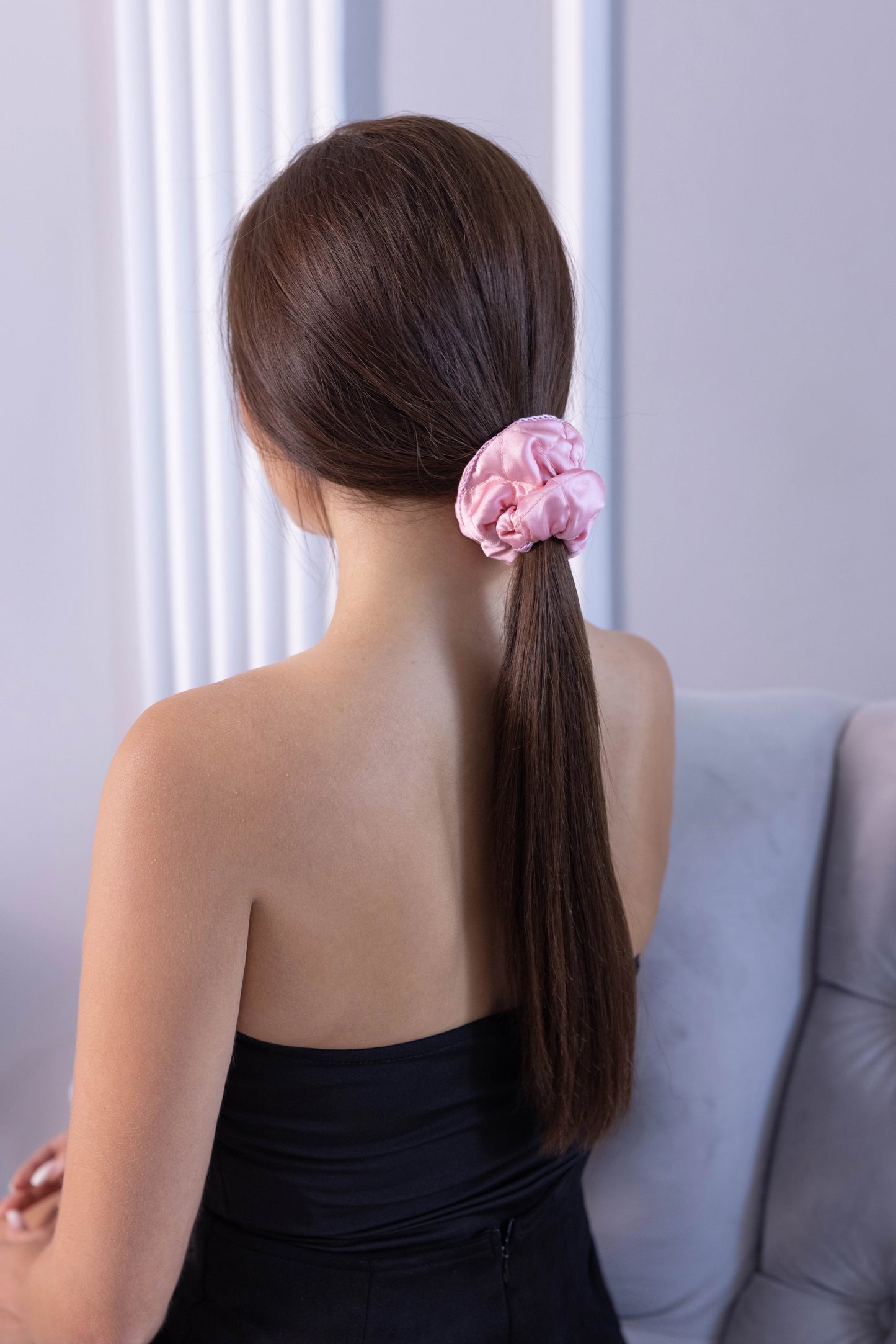 
                  
                    A dark-haired woman, view from the back, with stylish ponytail is wearing Malkiele designer pink silk scrunchie, embellished pink silk knit ribbon, name Morning Passion.
                  
                