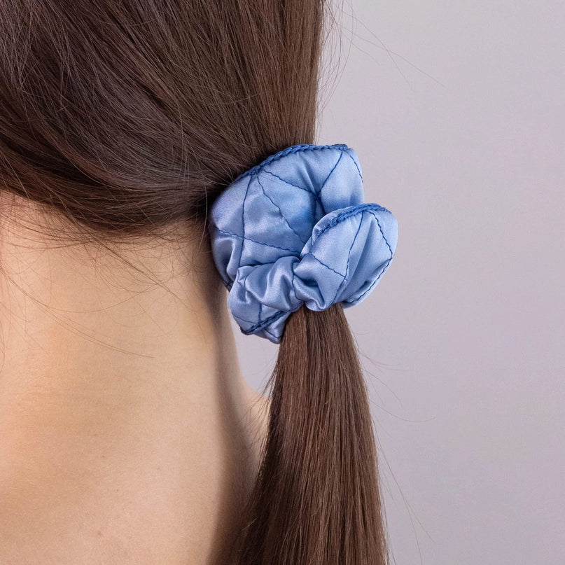 
                  
                    A dark-haired woman, view from the back, with stylish ponytail is wearing Malkiele designer light blue silk scrunchie, embellished blue silk knit ribbon, name Morning Passion.
                  
                