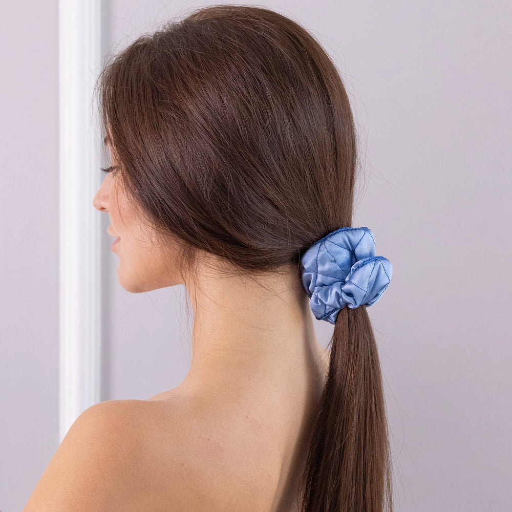 
                  
                    A dark-haired woman, view from the back, with stylish ponytail is wearing Malkiele designer light blue silk scrunchie, embellished blue silk knit ribbon, name Morning Passion.
                  
                