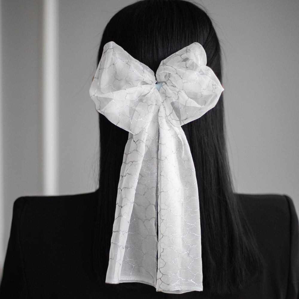 A dark-haired woman is wearing Malkiele Art Chiffon bow in white, name Romantic