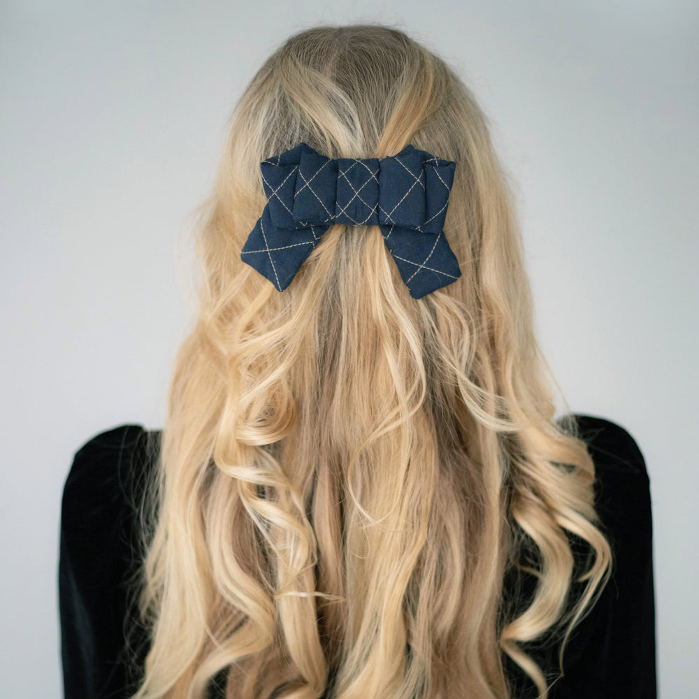 Blonde-haired girl in black dress from behind, is wearing Malkiele designer navy blue silk quilted bow, embellished with beige threads, name Seductive.