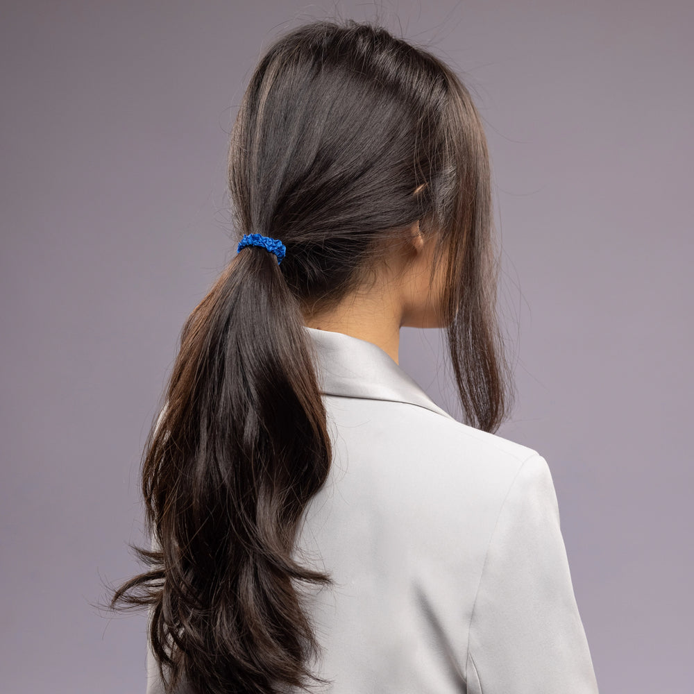 
                  
                    A black-haired woman in grey jacket, view from the back, with a stylish ponytail is wearing Malkiele designer royal blue silk hair tie, name Finesse.
                  
                