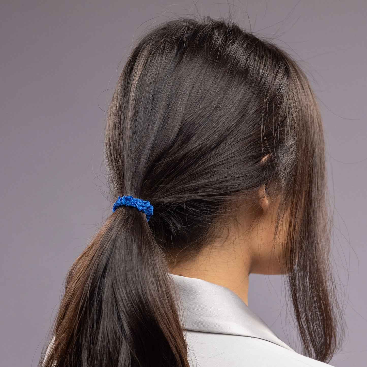 
                  
                    A black-haired woman, view from the back, with a stylish ponytail is wearing Malkiele designer royal blue silk hair tie, details, name Finesse.
                  
                