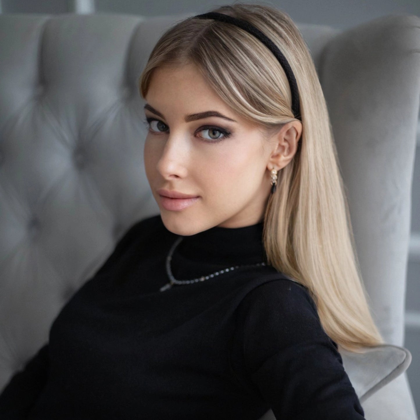 
                  
                    A blonde-haired girl in black turtleneck, looks at the camera, with flowing hair is wearing Malkiele designer black silk knit headband, name Virgin.
                  
                