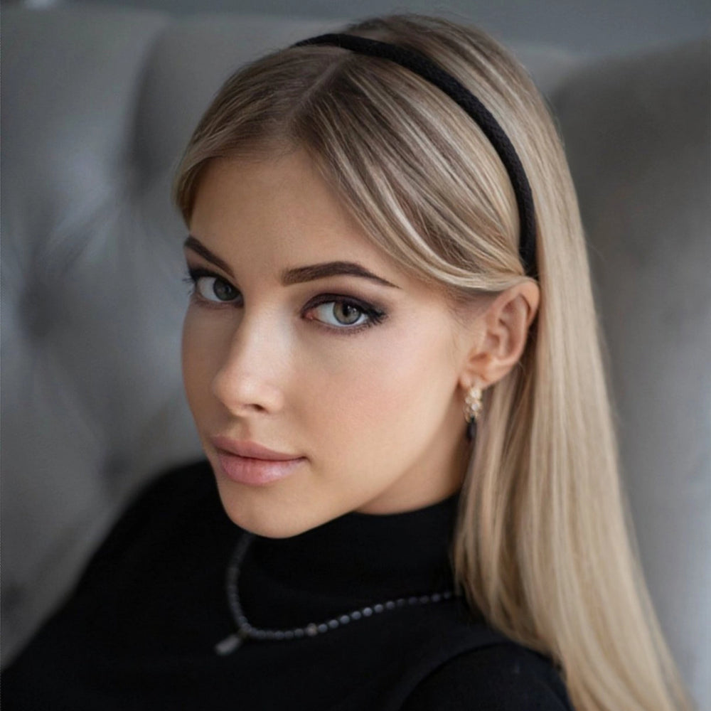 A blonde-haired girl in black turtleneck, looks at the camera, with flowing hair is wearing Malkiele designer black silk knit headband, name Virgin.