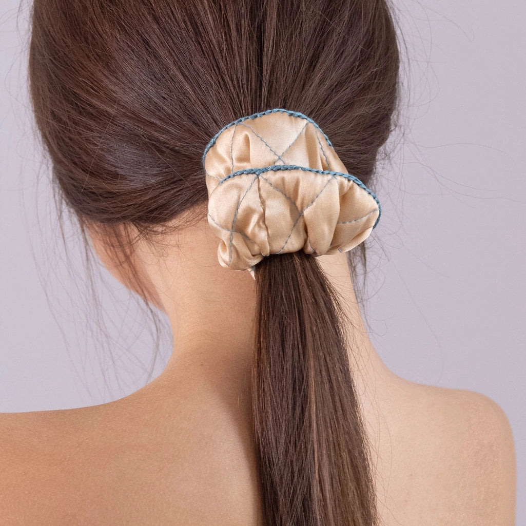 
                  
                    A dark-haired woman, view from the back, with stylish ponytail is wearing Malkiele designer beige silk scrunchie, embellished green silk knit ribbon, name Morning Passion.
                  
                