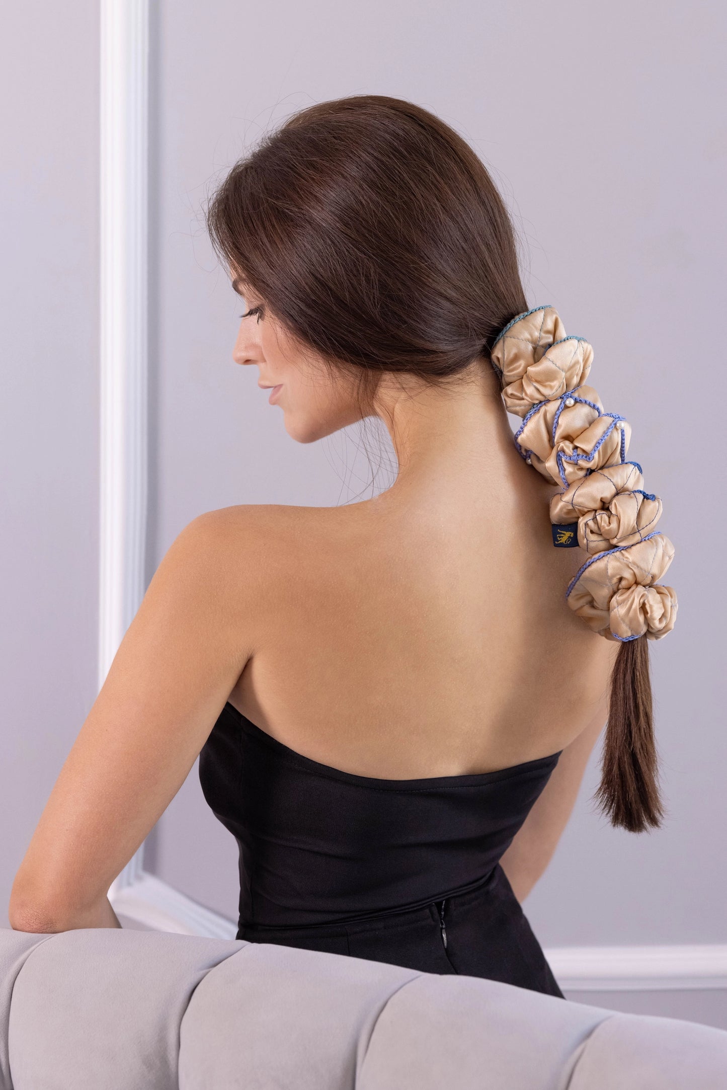 
                  
                    A dark-haired woman, side view, with stylish ponytail is wearing Malkiele designer beige silk scrunchies set, embellished green silk knit ribbon, name Morning Passion.
                  
                