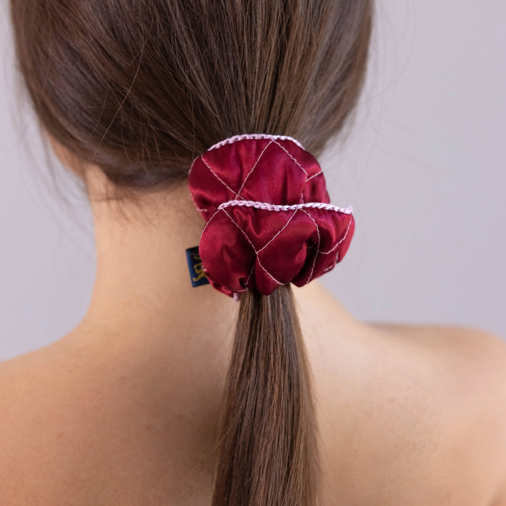 
                  
                    A dark-haired woman, view from the back, with stylish ponytail is wearing Malkiele designer burgundy silk scrunchie, embellished pink silk knit ribbon, name Morning Passion.
                  
                