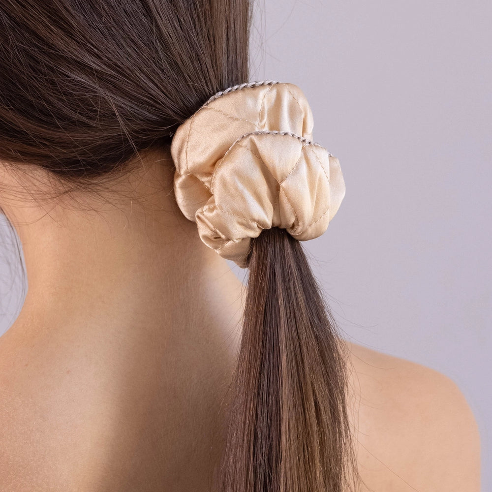 
                  
                    A dark-haired woman, view from the back, scrunchie details, with long and stylish ponytail is wearing Malkiele designer beige silk quilted scrunchie, embellished with beige silk knit ribbon, name Morning Passion.
                  
                