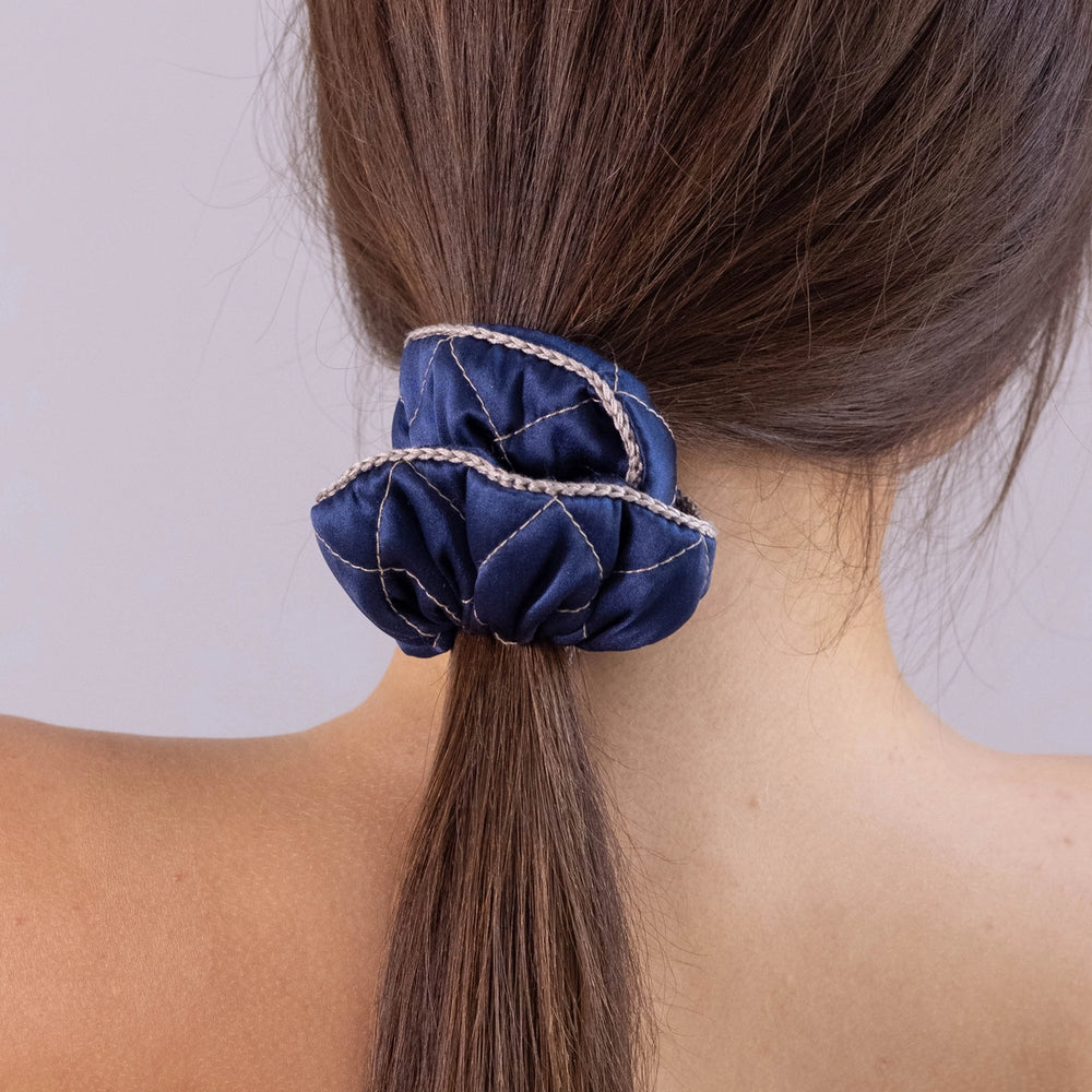 
                  
                    A dark-haired woman, view from the back, showing scrunchie details, with long and stylish ponytail is wearing Malkiele designer navy blue silk quilted scrunchie, embellished with beige silk knit ribbon, name Morning Passion.
                  
                