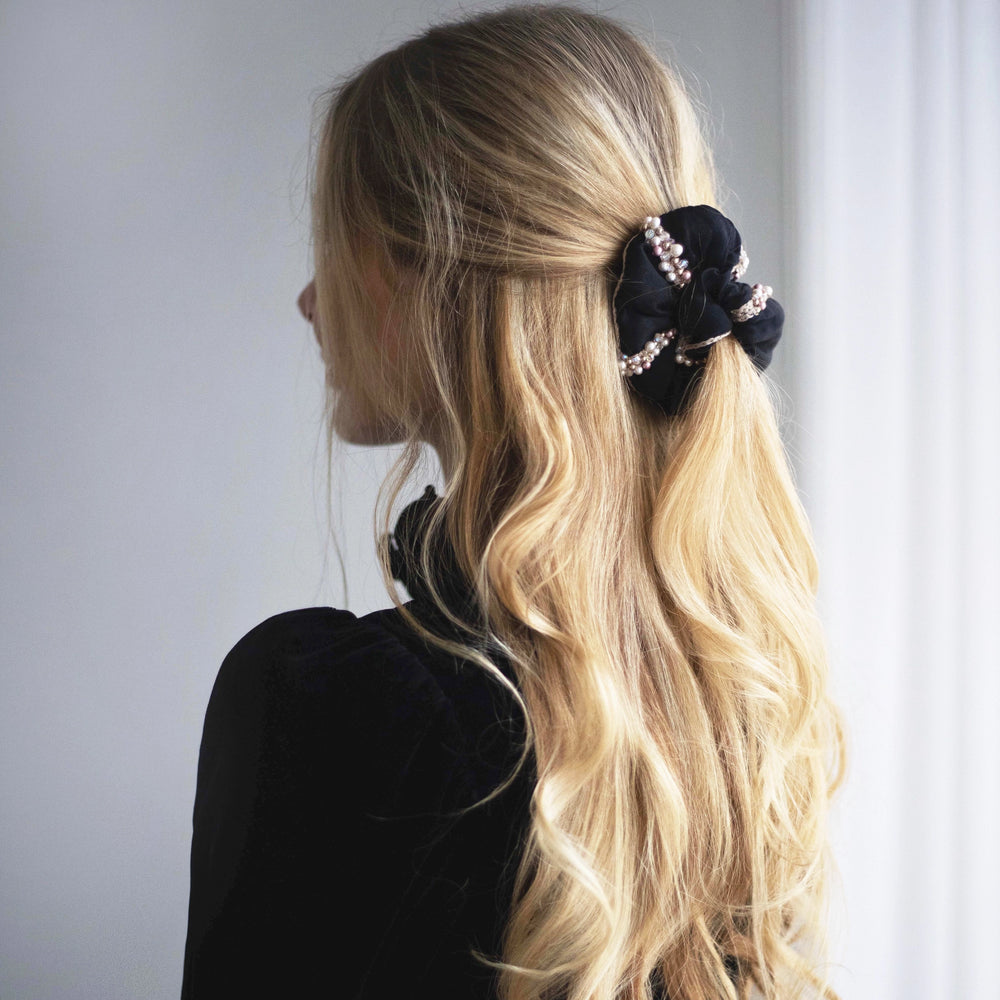 
                  
                    A blonde-haired girl in black dress, with stylish ponytail is wearing Malkiele designer black silk scrunchie, embellished with crystals from Swarovski® and beige silk knit ribbon, name Elizabeth.
                  
                