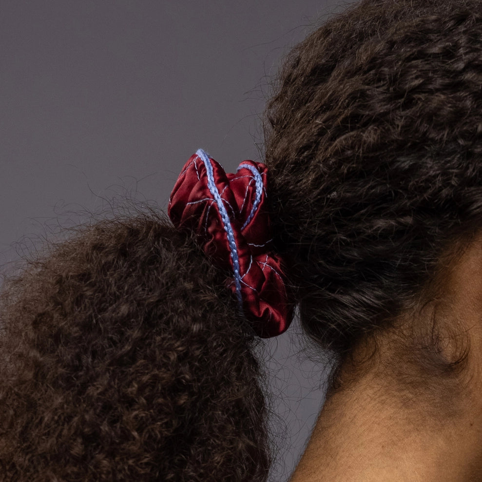 
                  
                    An African woman's ponytail, view from the side, is wearing Malkiele designer burgundy quilted silk scrunchie, embellished with light blue silk knit ribbon, details, name Morning Passion
                  
                