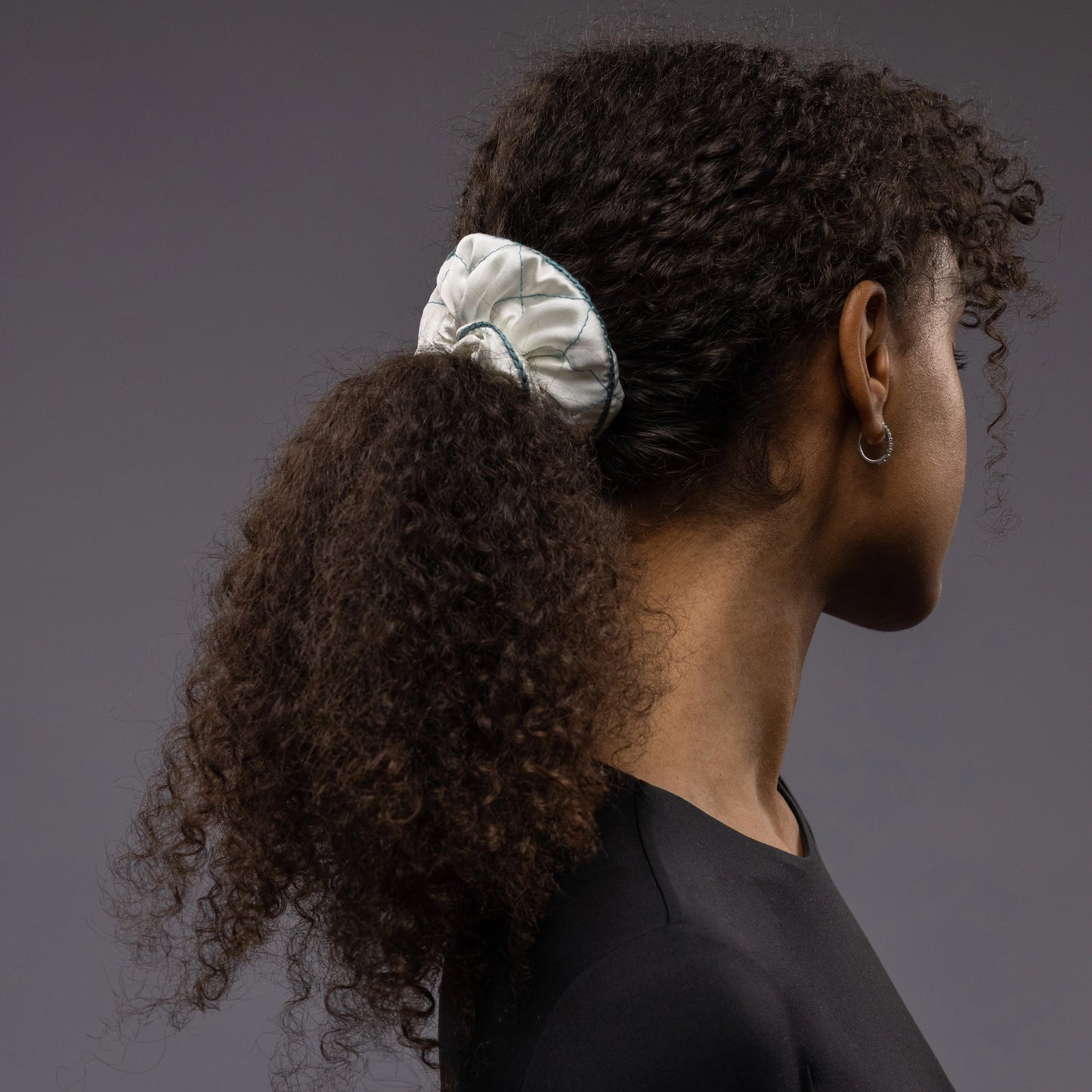 
                  
                    An African dark-haired woman, view from the side, with a stylish ponytail is wearing Malkiele designer white quilted silk scrunchie, embellished with green silk knit ribbon, name Morning Passion
                  
                