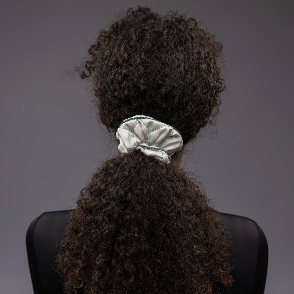 
                  
                    An African dark-haired woman, view from the back, with a stylish ponytail is wearing Malkiele designer white quilted silk scrunchie, embellished with green silk knit ribbon, name Morning Passion
                  
                