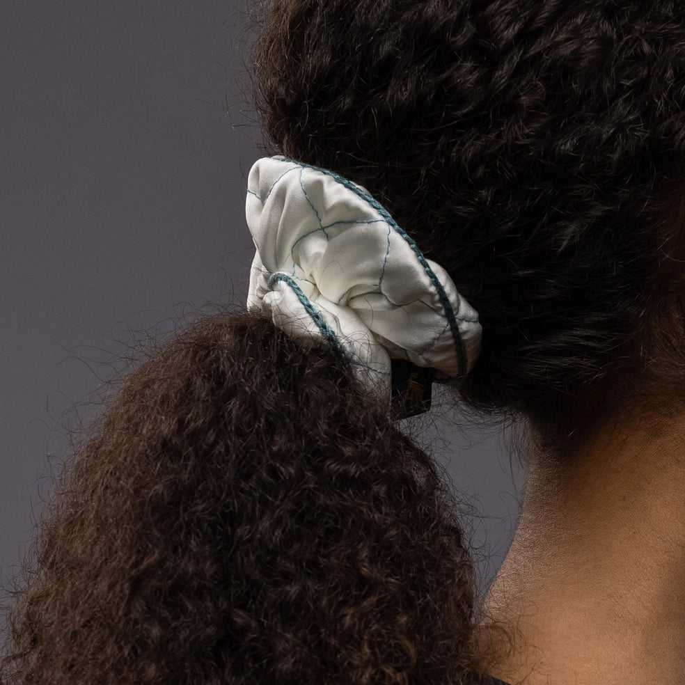 
                  
                    An African dark-haired woman, view from the back, with a stylish ponytail is wearing Malkiele designer white quilted silk scrunchie, embellished with green silk knit ribbon, details,name Morning Passion
                  
                