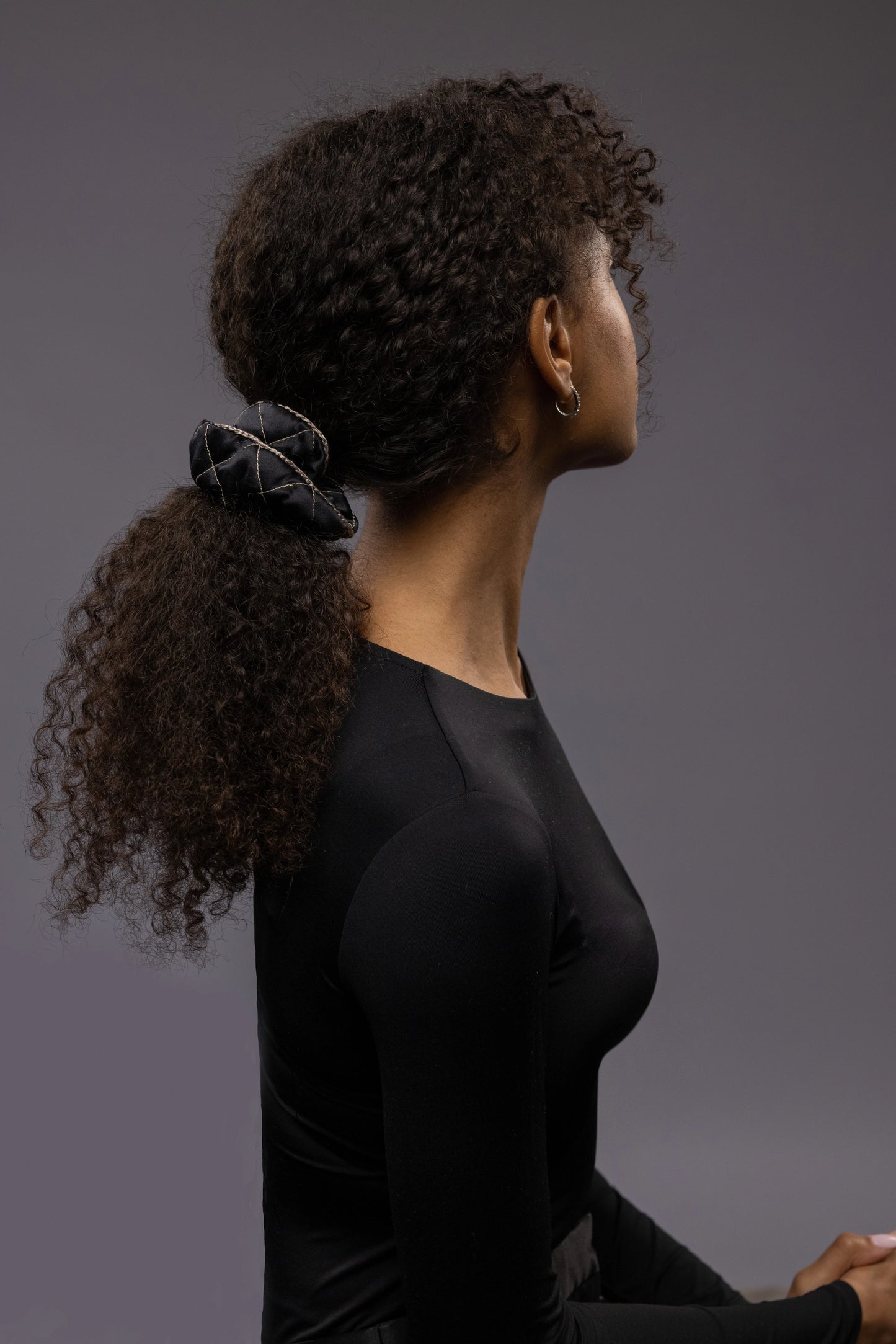 
                  
                    An African dark-haired woman, view from the back, with a stylish ponytail is wearing Malkiele designer black quilted silk scrunchie, embellished with beige silk knit ribbon, name Morning Passion
                  
                