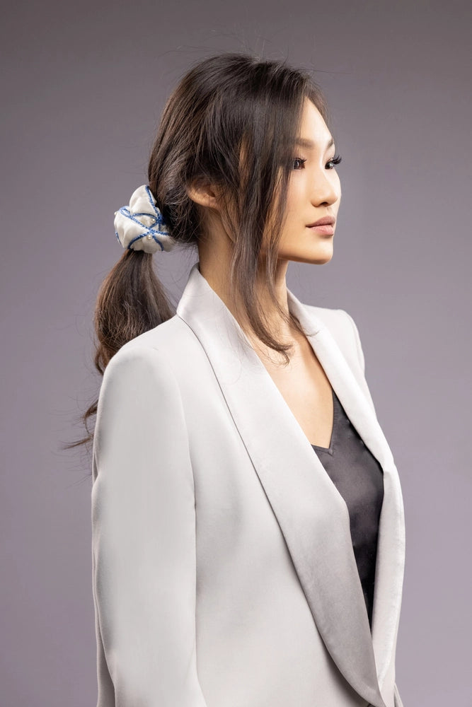 
                  
                    Asian smiling woman in grey jacket, front view, with a stylish ponytail is wearing Malkiele designer white silk scrunchie, embellished with white pearls and light blue silk knit ribbon, name Majestic.
                  
                