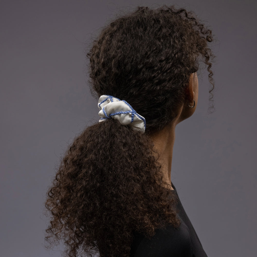 
                  
                    African woman, the view from the back, with a stylish ponytail is wearing Malkiele designer white silk scrunchie, embellished with white pearls and light blue silk knit ribbon, name Majestic.
                  
                