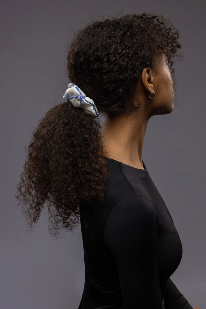 
                  
                    African woman, the view from the side, with a stylish ponytail is wearing Malkiele designer white silk scrunchie, embellished with white pearls and light blue silk knit ribbon, name Majestic.
                  
                