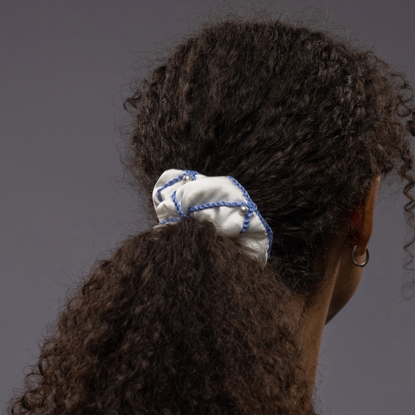 
                  
                    African woman, the view from the back, with a stylish ponytail is wearing Malkiele designer white silk scrunchie, embellished with white pearls and light blue silk knit ribbon, name Majestic.
                  
                