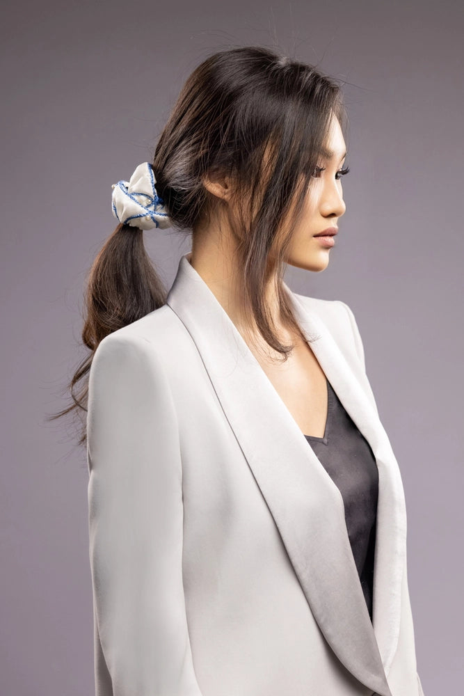 
                  
                    Asian woman in grey jacket, front view, with a stylish ponytail is wearing Malkiele designer white silk scrunchie, embellished with white pearls and light blue silk knit ribbon, name Majestic.
                  
                