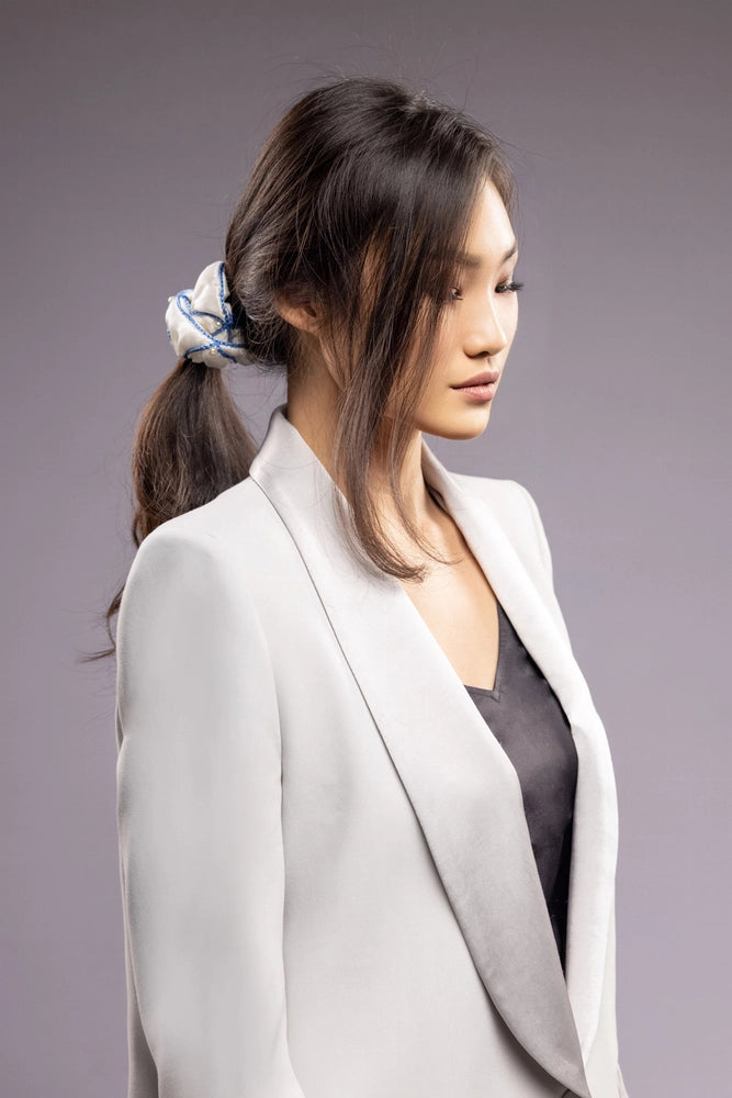 
                  
                    Asian woman in grey jacket, front view, with a stylish ponytail is wearing Malkiele designer white silk scrunchie, embellished with white pearls and light blue silk knit ribbon, name Majestic.
                  
                