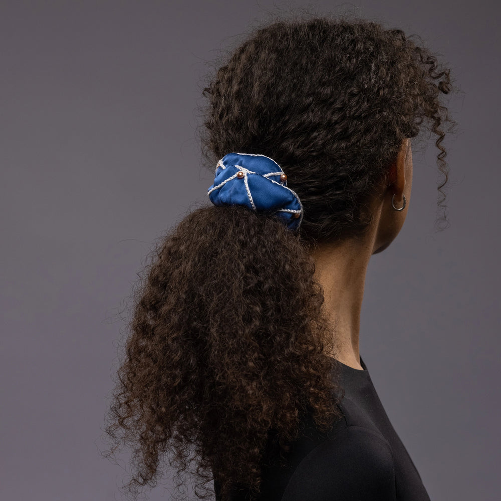 African woman, back view, with a stylish ponytail is wearing Malkiele designer royal blue silk scrunchie, embellished with gold pearls and white silk knit ribbon, name Majestic.