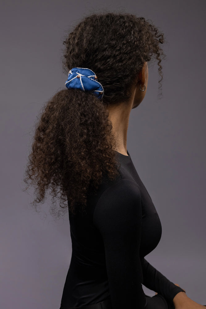 
                  
                    African woman, back view, with a stylish ponytail is wearing Malkiele designer royal blue silk scrunchie, embellished with gold pearls and white silk knit ribbon, name Majestic.
                  
                