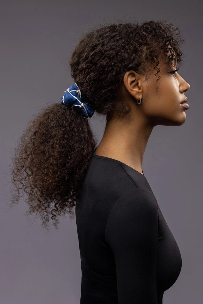 
                  
                    African woman, side view, with a stylish ponytail is wearing Malkiele designer royal blue silk scrunchie, embellished with gold pearls and white silk knit ribbon, name Majestic.
                  
                