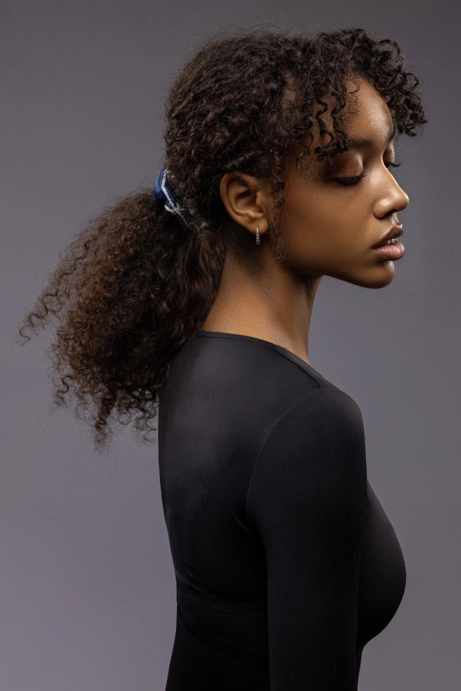 
                  
                    African woman, side view, with a stylish ponytail is wearing Malkiele designer royal blue silk scrunchie, embellished with gold pearls and white silk knit ribbon, name Majestic.
                  
                