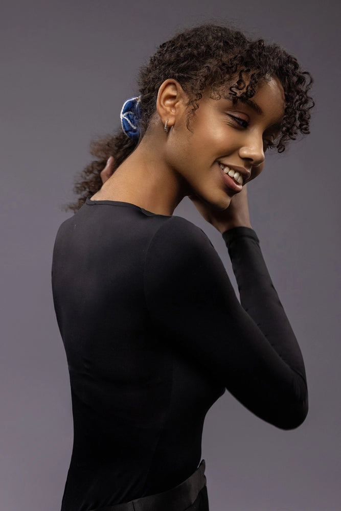 
                  
                    Smiling African woman, front view, with a stylish ponytail is wearing Malkiele designer royal blue silk scrunchie, embellished with gold pearls and white silk knit ribbon, name Majestic.
                  
                