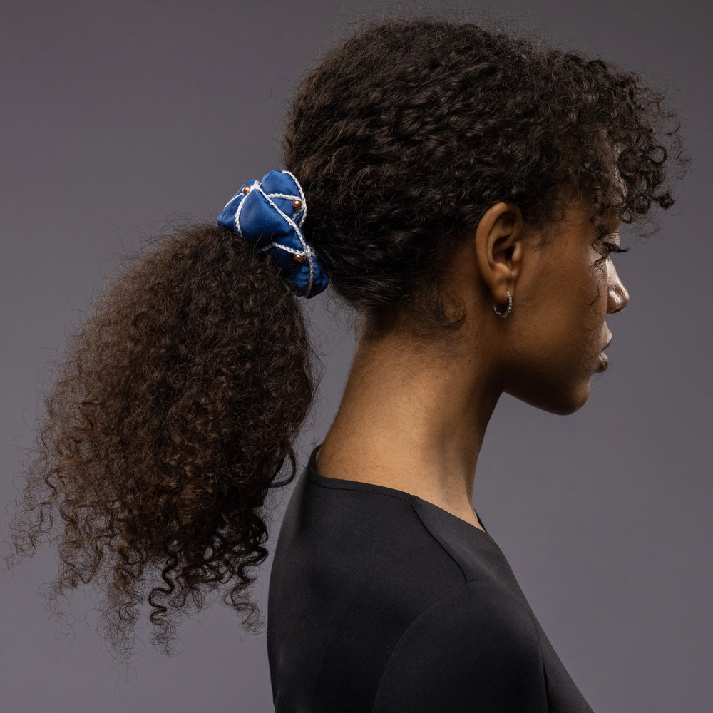 
                  
                    African woman, side view, with a stylish ponytail is wearing Malkiele designer royal blue silk scrunchie, embellished with gold pearls and white silk knit ribbon, name Majestic.
                  
                