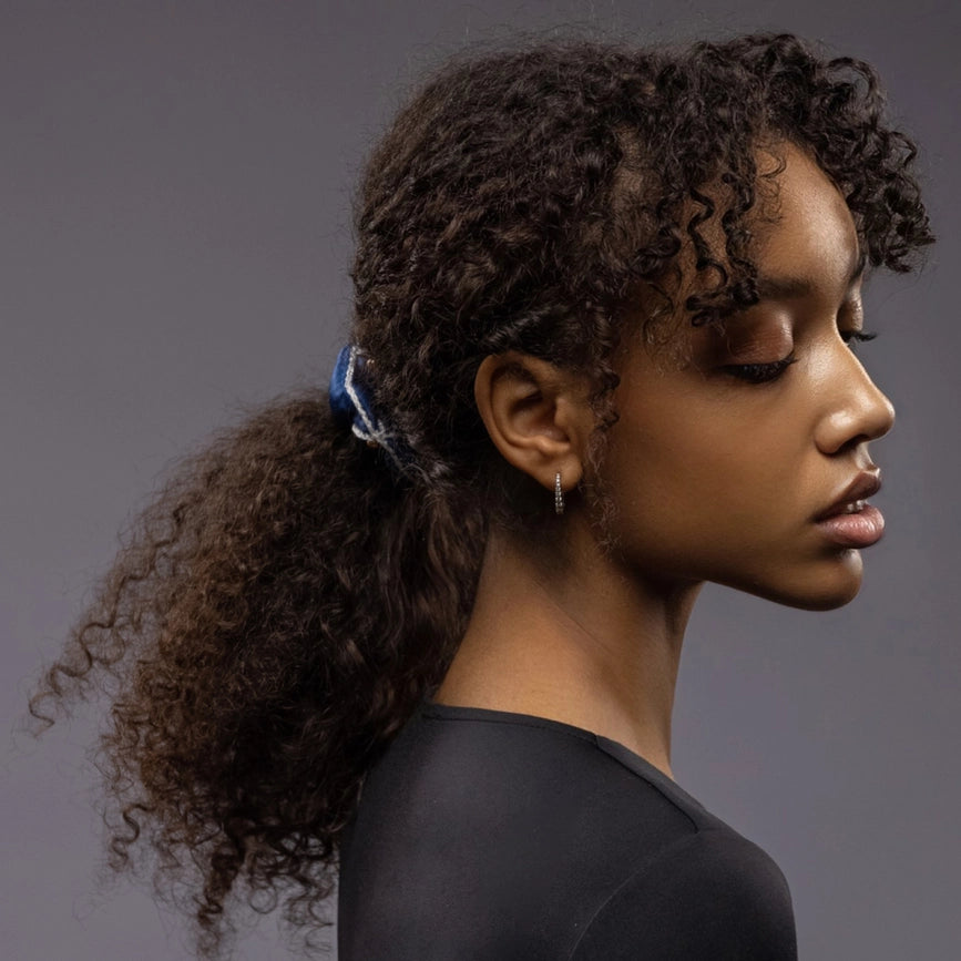 
                  
                    African woman, front view, with a stylish ponytail is wearing Malkiele designer royal blue silk scrunchie, embellished with gold pearls and white silk knit ribbon, name Majestic.
                  
                