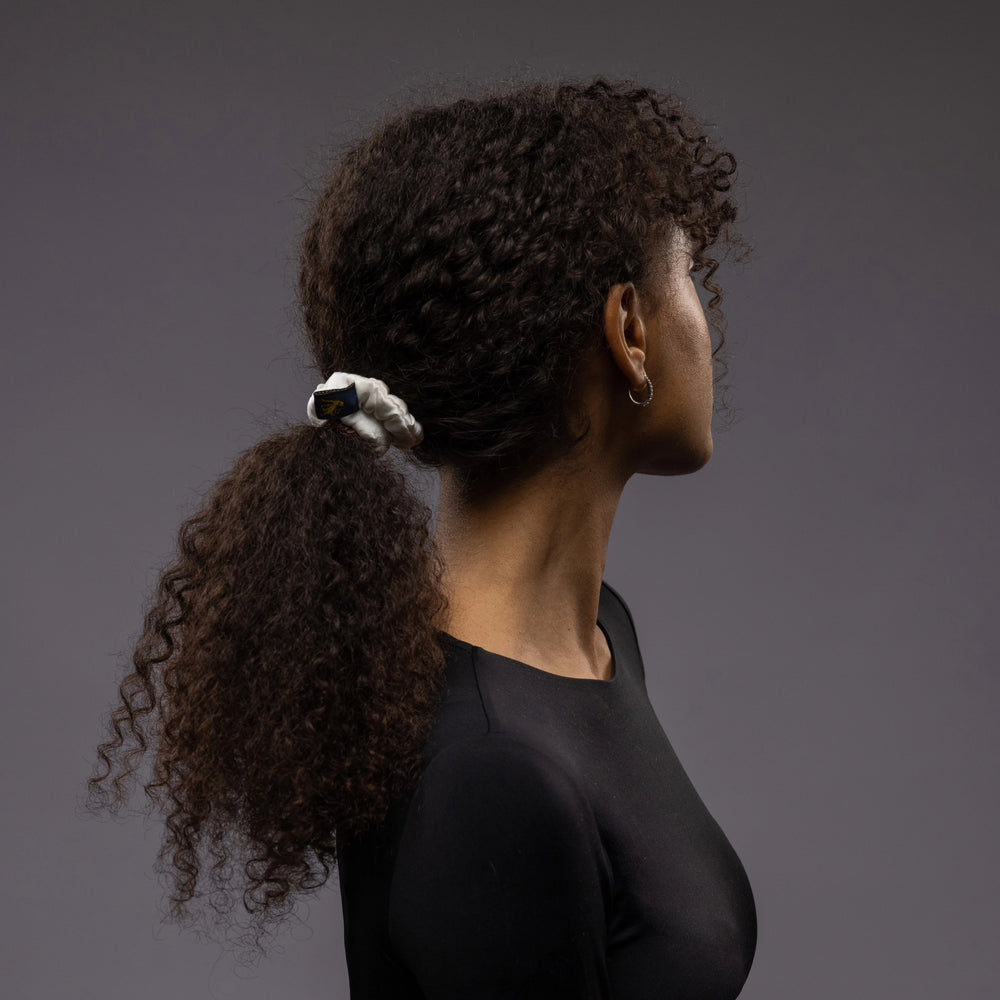 
                  
                    A dark-haired woman, side view, with stylish ponytail is wearing Malkiele designer white silk-covered coil scrunchie, name Grace.
                  
                