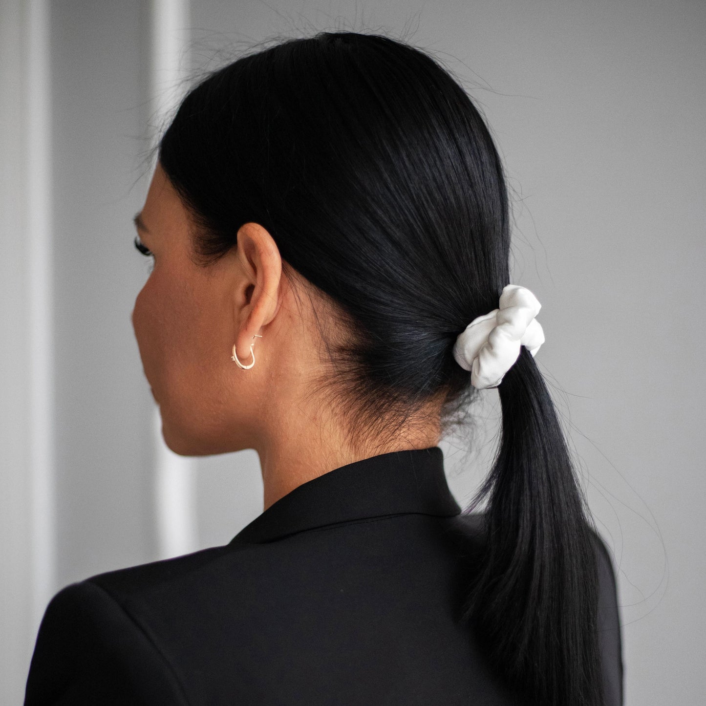 
                  
                    A dark-haired woman, view from the back, with stylish ponytail is wearing Malkiele designer white silk-covered coil scrunchie, name Grace.
                  
                